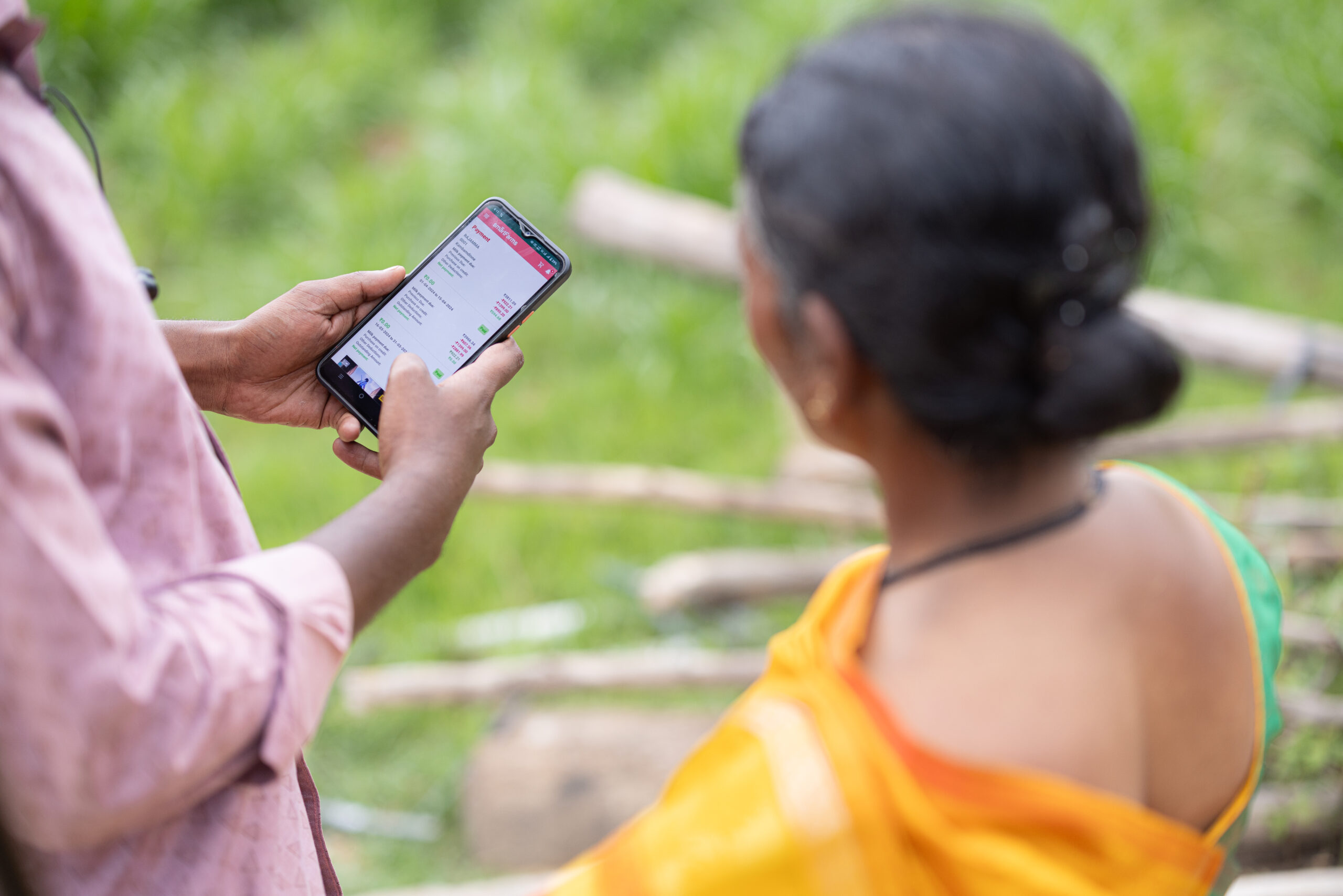 Sakkamma receives assistance on a mobile phone from a loan officer.
